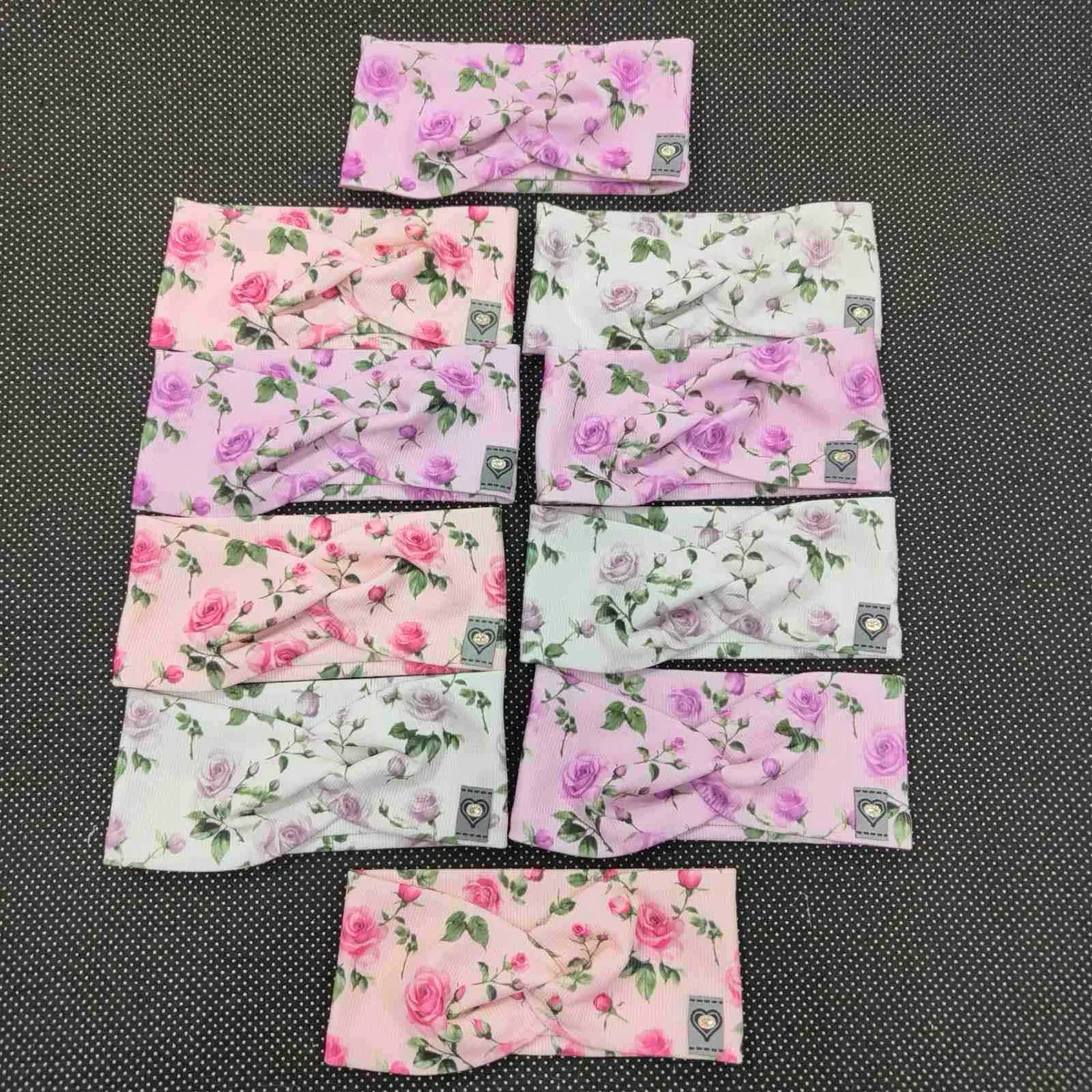 dziesięć dziecięcych opasek w pastelowych kolorach z nadrukiem róż na czarnym tle
