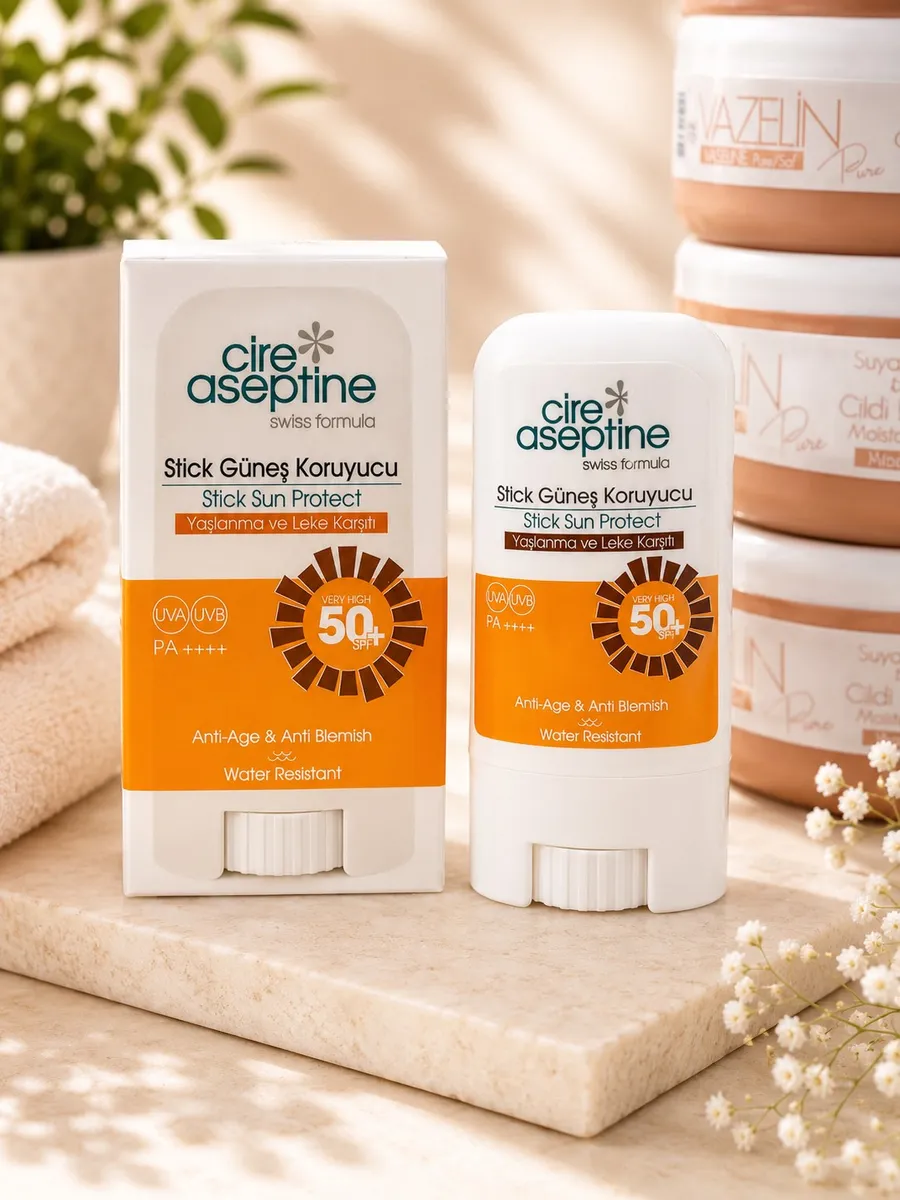 Biały sztyft i opakowanie Cire Aseptine Stick Sun Protect SPF 50+ PA++++ z pomarańczowymi etykietami na marmurowym blacie obo
