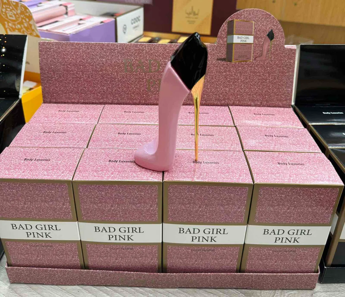 Perfumy Bad Girl Pink 30ml w różowo-złotym flakonie w kształcie szpilki na tle różowych pudełek