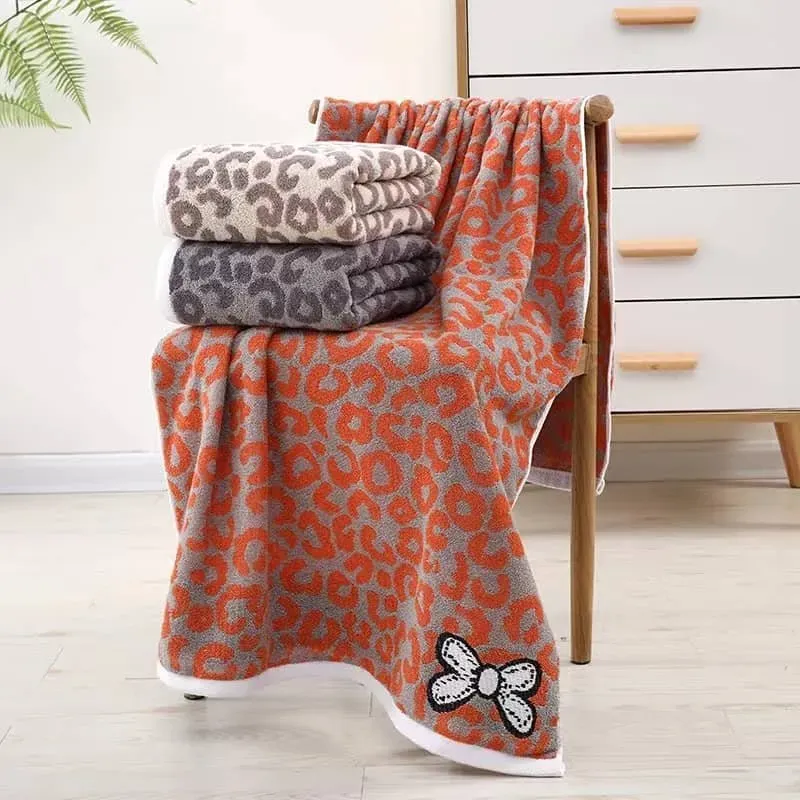 Złożone ręczniki z mikrofibry w szarym kolorze z pomarańczowym wzorem leopard print, jeden rozłożony na krześle z widoczną ap