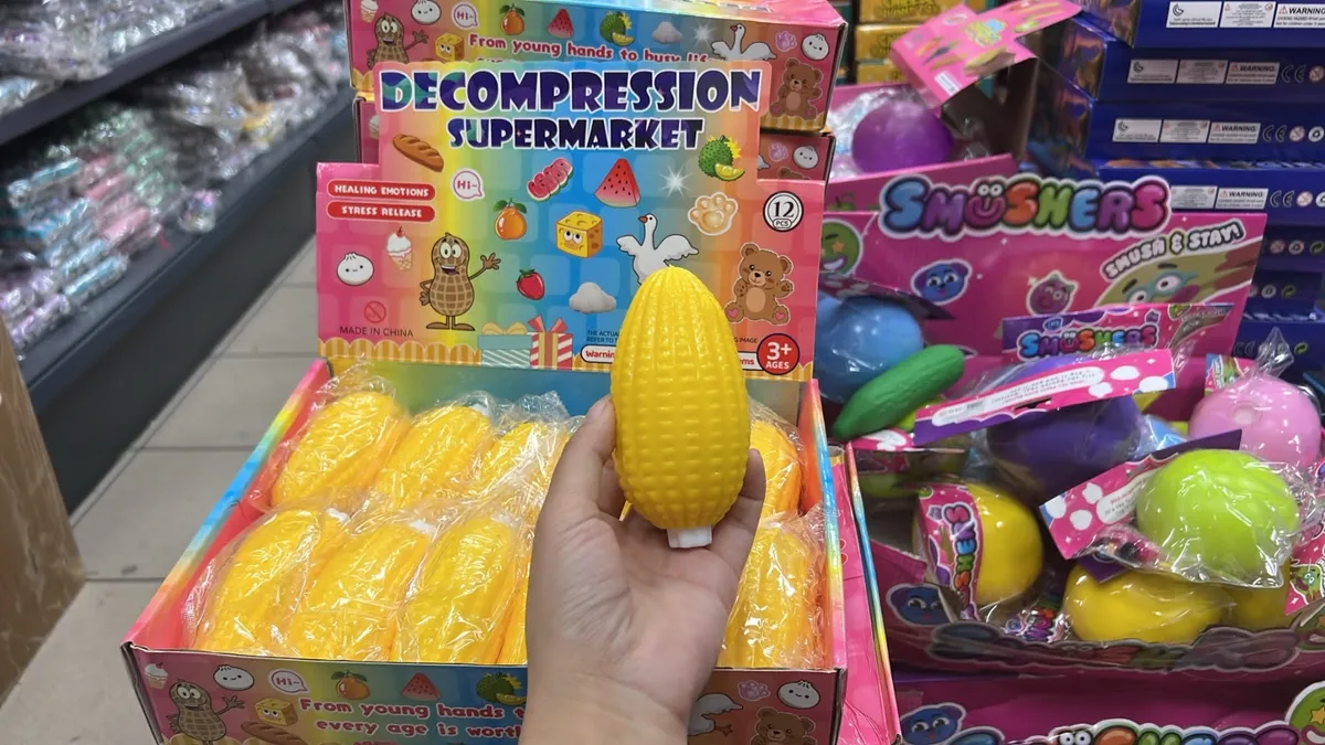 Żółta kukurydza antystresowa trzymana w dłoni na tle kolorowego kartonu zbiorczego z serii Decompression Supermarket