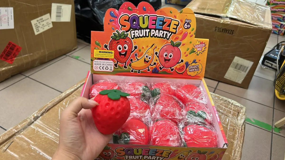 Ręka trzymająca czerwoną piankową truskawkę z zielonym listkiem z opakowania Squeeze Fruit Party