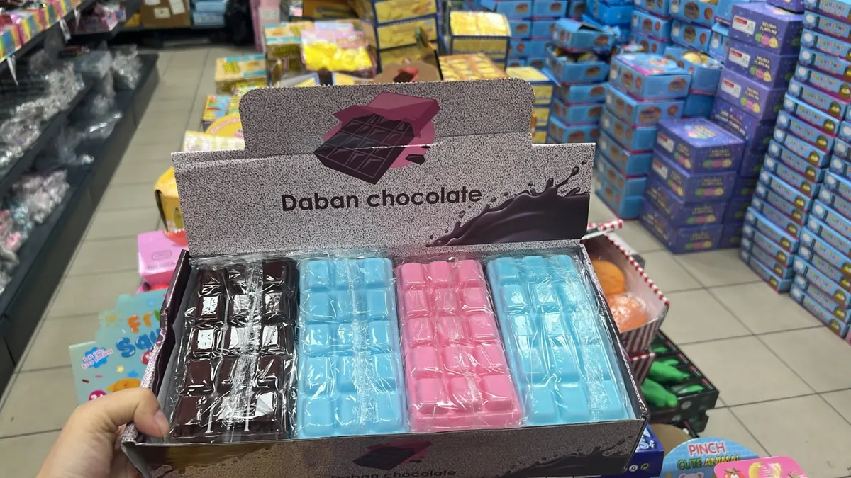 Ręka trzyma otwarte kartonowe pudełko z czterema kolorowymi tabliczkami czekolady Daban Chocolate: brązową, błękitną, różową