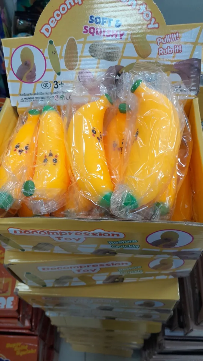 Żółte banany squishy w foliowych opakowaniach z uśmiechniętymi buźkami, wystawione w żółtym kartonowym displayu z napisami So