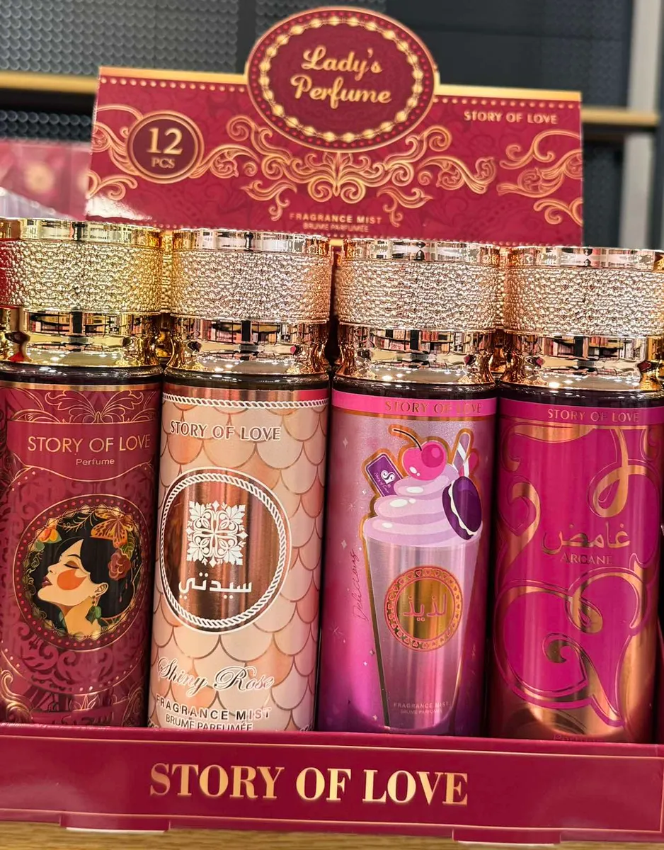 Zestaw czterech kolorowych butelek body mist Story of Love 90ml z ozdobnymi złotymi nakrętkami na czerwonym stojaku ekspozycy