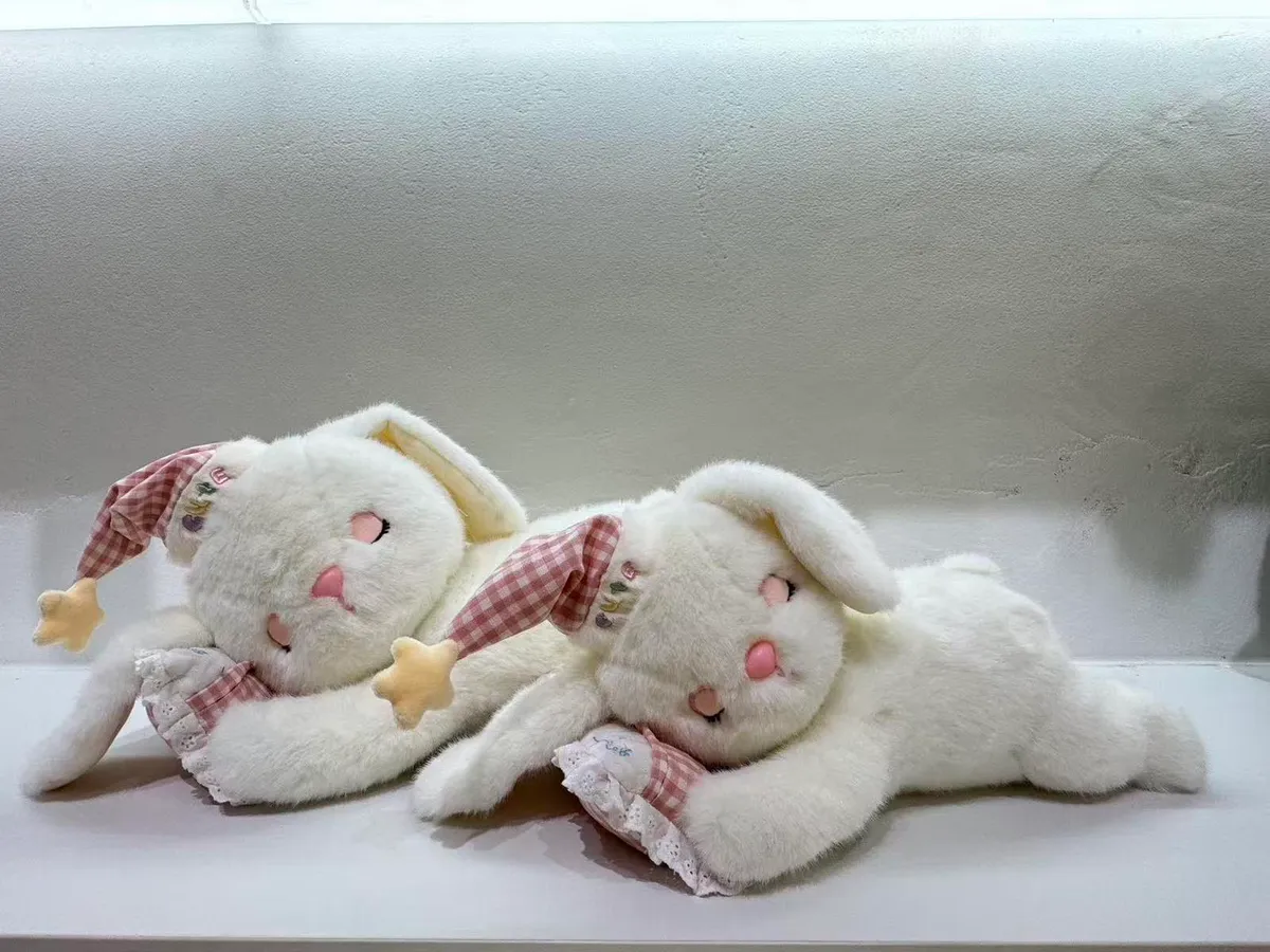Dwa białe pluszowe króliczki w czerwono-białej kratce leżące na boku z poduszeczkami