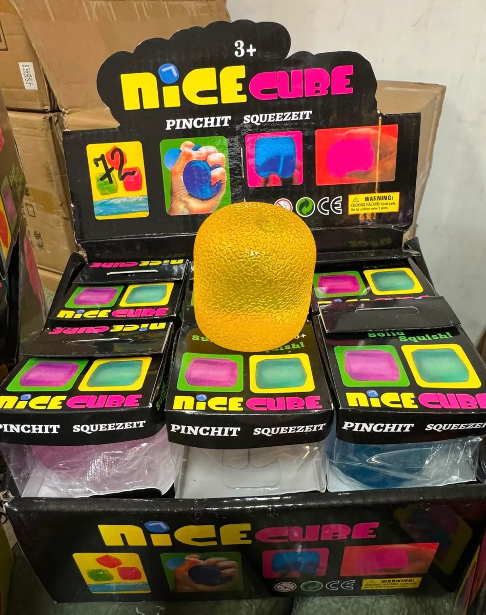 Żółty Nice Cube antystresowy w displayu z czarnym kartonem, widoczne opakowania w innych kolorach, oznaczenie 3+ i instrukcje