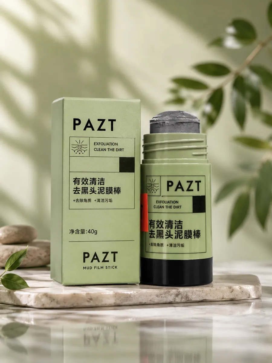 PAZT Mud Film Stick 40g w szałwiowo-czarnym opakowaniu obok pudełka, na marmurowej podstawce z liśćmi i kamieniami