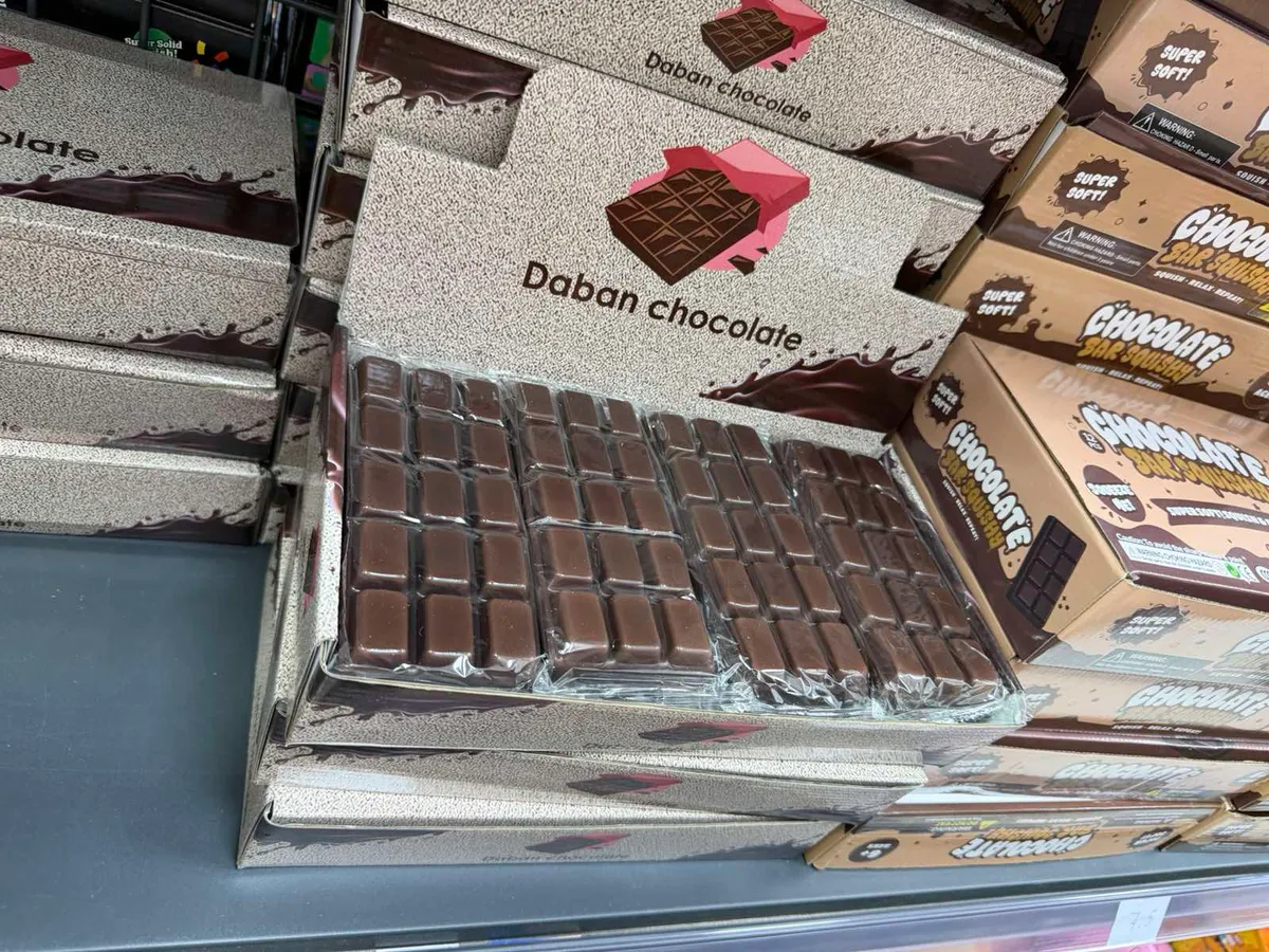 Karton display z kostkami czekolady mlecznej Daban Chocolate w foliowych opakowaniach, srebrzyste pudełko z grafiką tabliczki