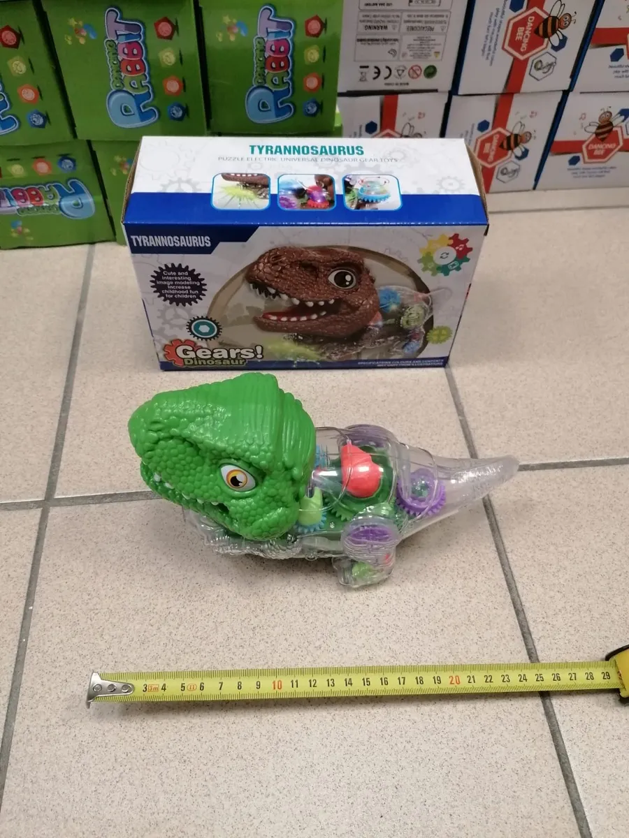 Zielony tyranozaur z przezroczystym korpusem odsłaniającym kolorowe tryby, obok pudełka z napisem Gears! Dinosaur, miarka pok