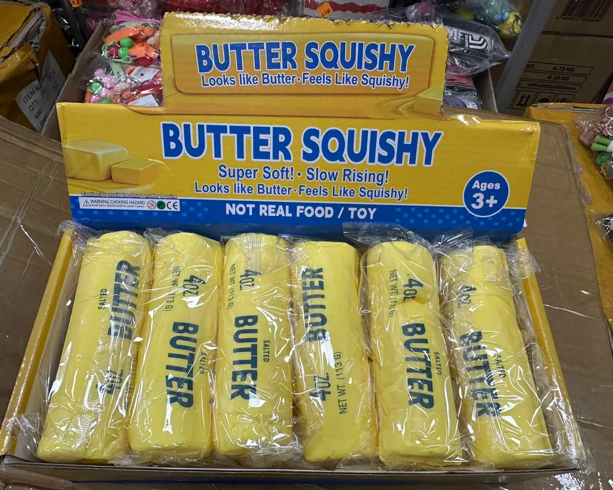 Żółte squishy w kształcie kostek masła solonego zapakowane w folię, w żółtym kartonie z napisem Butter Squishy