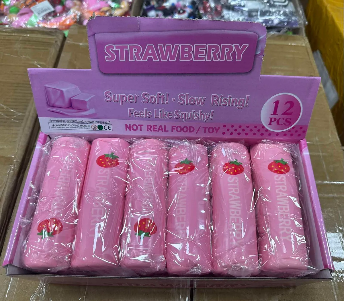 Różowe squishy w kształcie wałków z nadrukiem truskawki, zapakowane w fioletowe kartonowe opakowanie z napisem Strawberry Sup