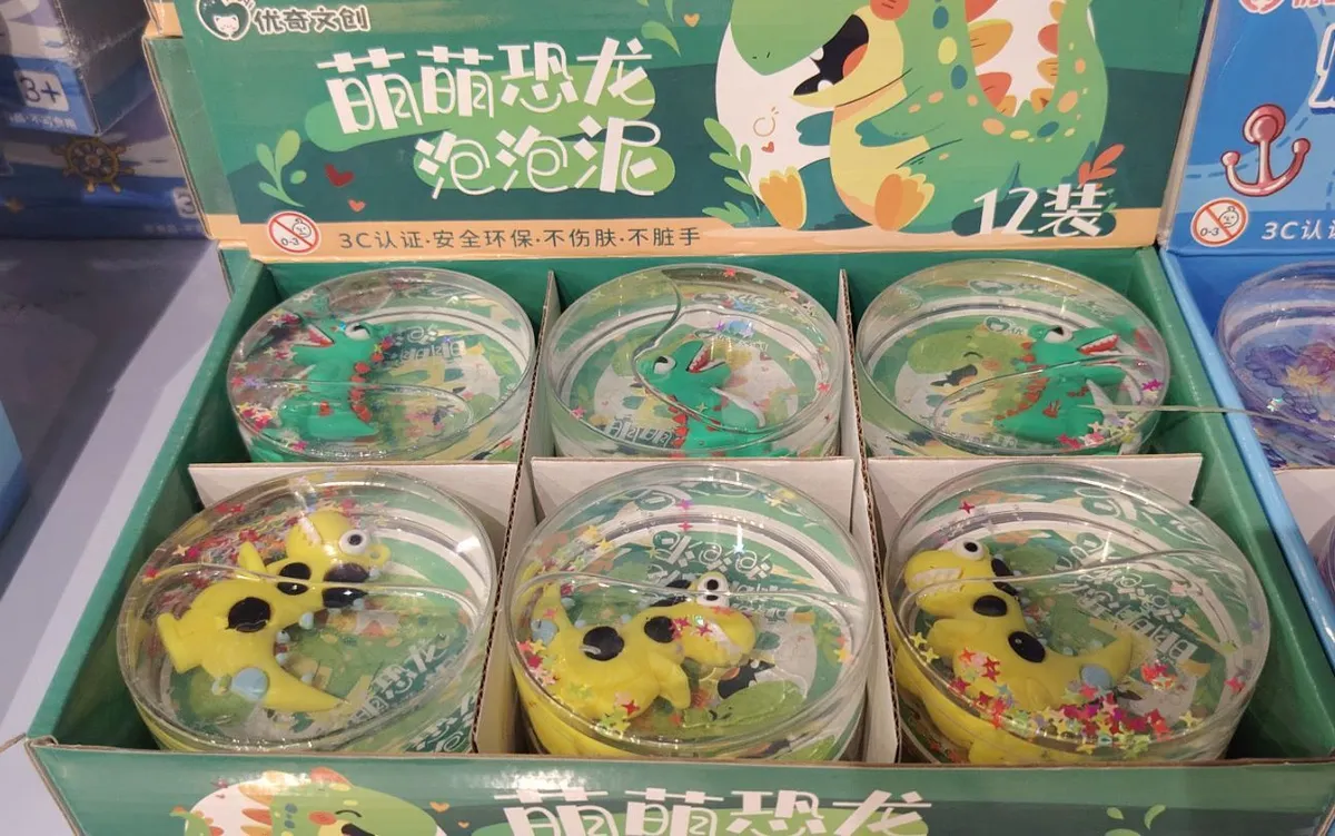 przezroczysty slime z zielonym i żółtym dinozaurem oraz brokatem w plastikowych pojemnikach