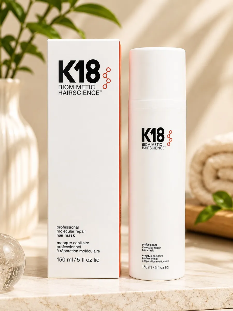 Biała butelka i opakowanie maski do włosów K18 Biomimetic Hairscience na marmurowym blacie
