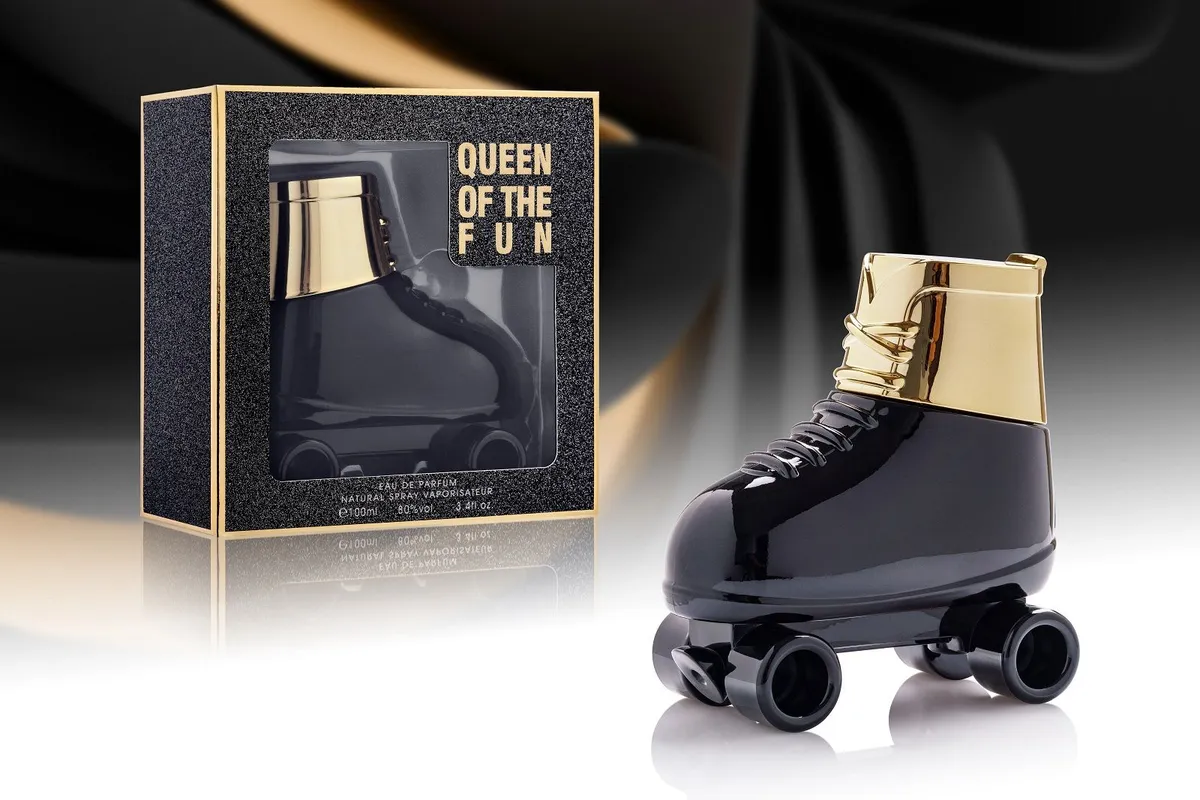 Czarny flakon perfum w kształcie rolki z złotymi elementami obok czarno-złotego pudełka z napisem Queen of the Fun