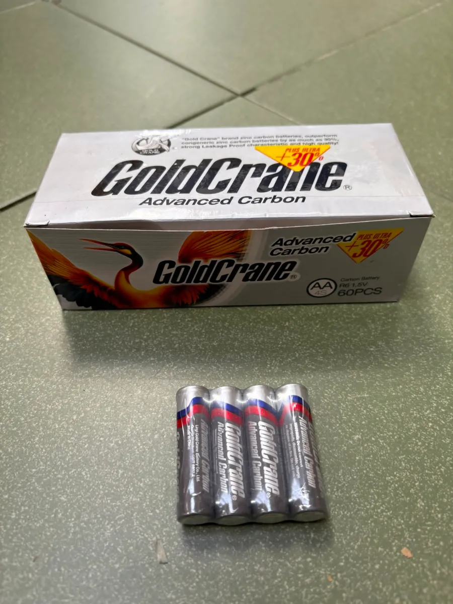 Opakowanie 60 sztuk baterii AA GoldCrane Advanced Carbon oraz cztery baterie na tle zielonej powierzchni