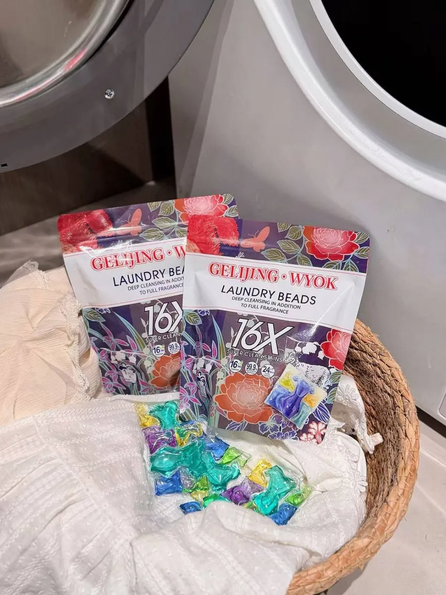 Kolorowe kapsułki do prania w koszu z białą tkaniną obok pralki, opakowania z kwiatowym wzorem