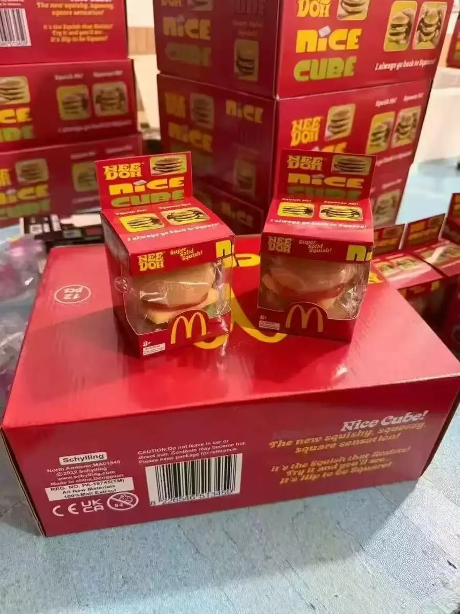 Miękka zabawka squishy hamburger McDonald's w czerwonym opakowaniu na tle kartonów