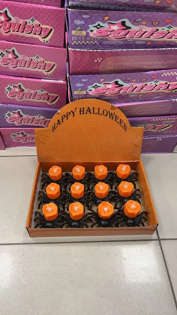 Pomarańczowe świeczki z białym knotem na czarnej podstawie pająka w kartonie z napisem Happy Halloween