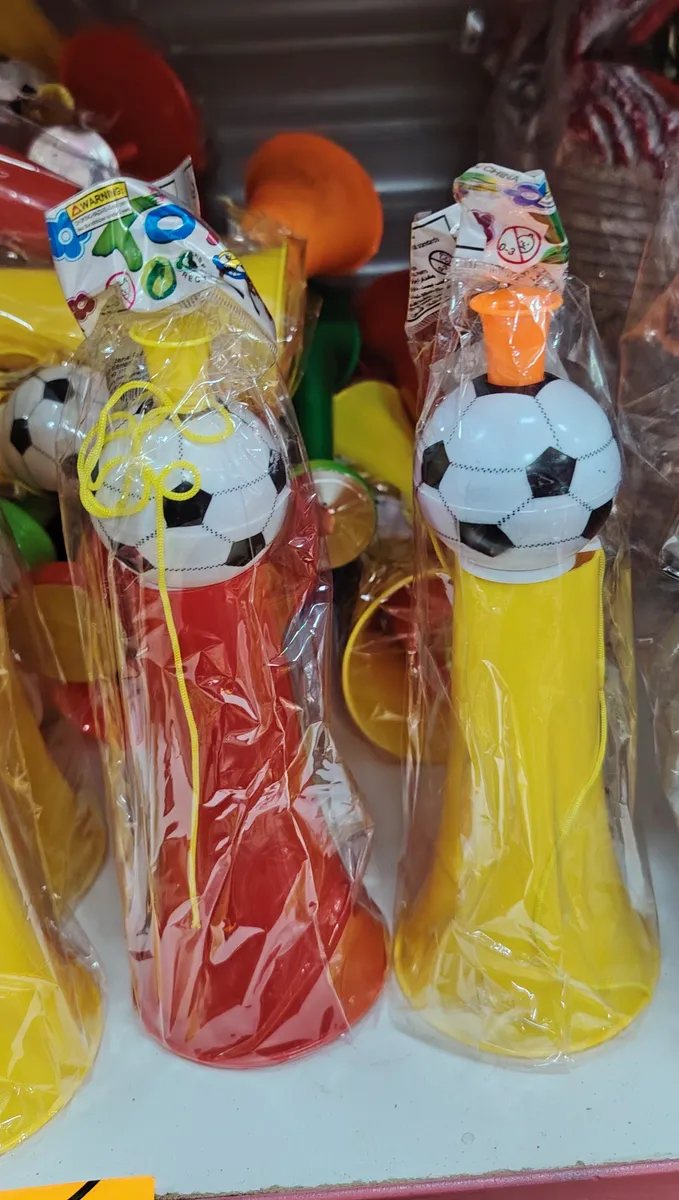 Plastikowa trąbka w kolorze czerwonym i żółtym z piłką nożną na górze, zapakowana w folię