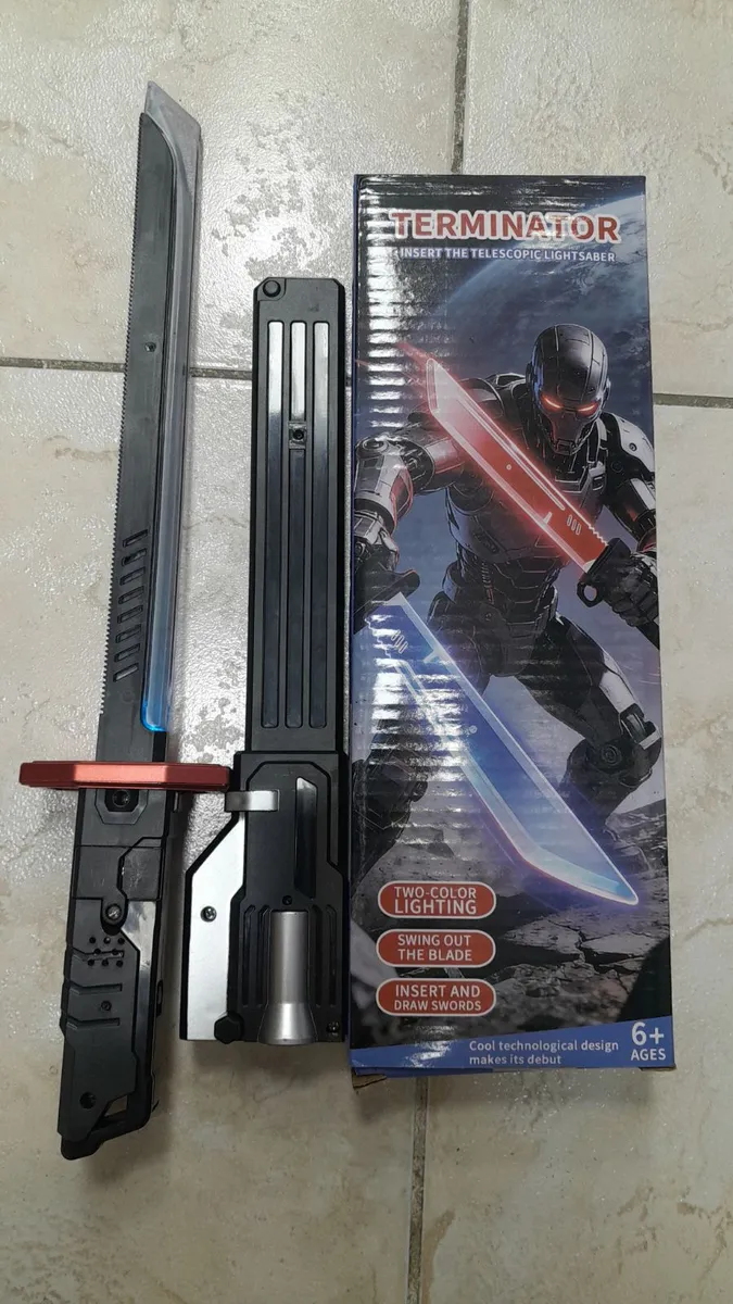 Zabawka miecz świetlny terminator z czarną rękojeścią i dwukolorowym ostrzem obok opakowania z grafiką robota