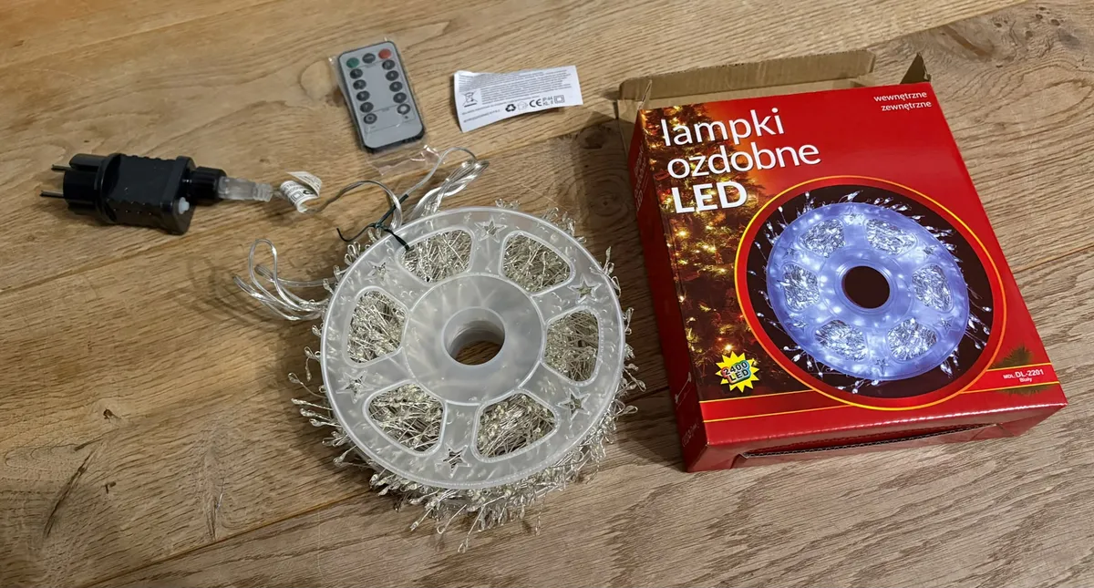 Lampki ozdobne LED na białym druciku z pilotem i zasilaczem oraz opakowanie na drewnianym stole