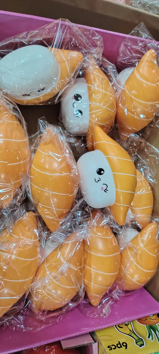 Pomarańczowe squishy w kształcie sushi z białym spodem i buźką, zapakowane w folię