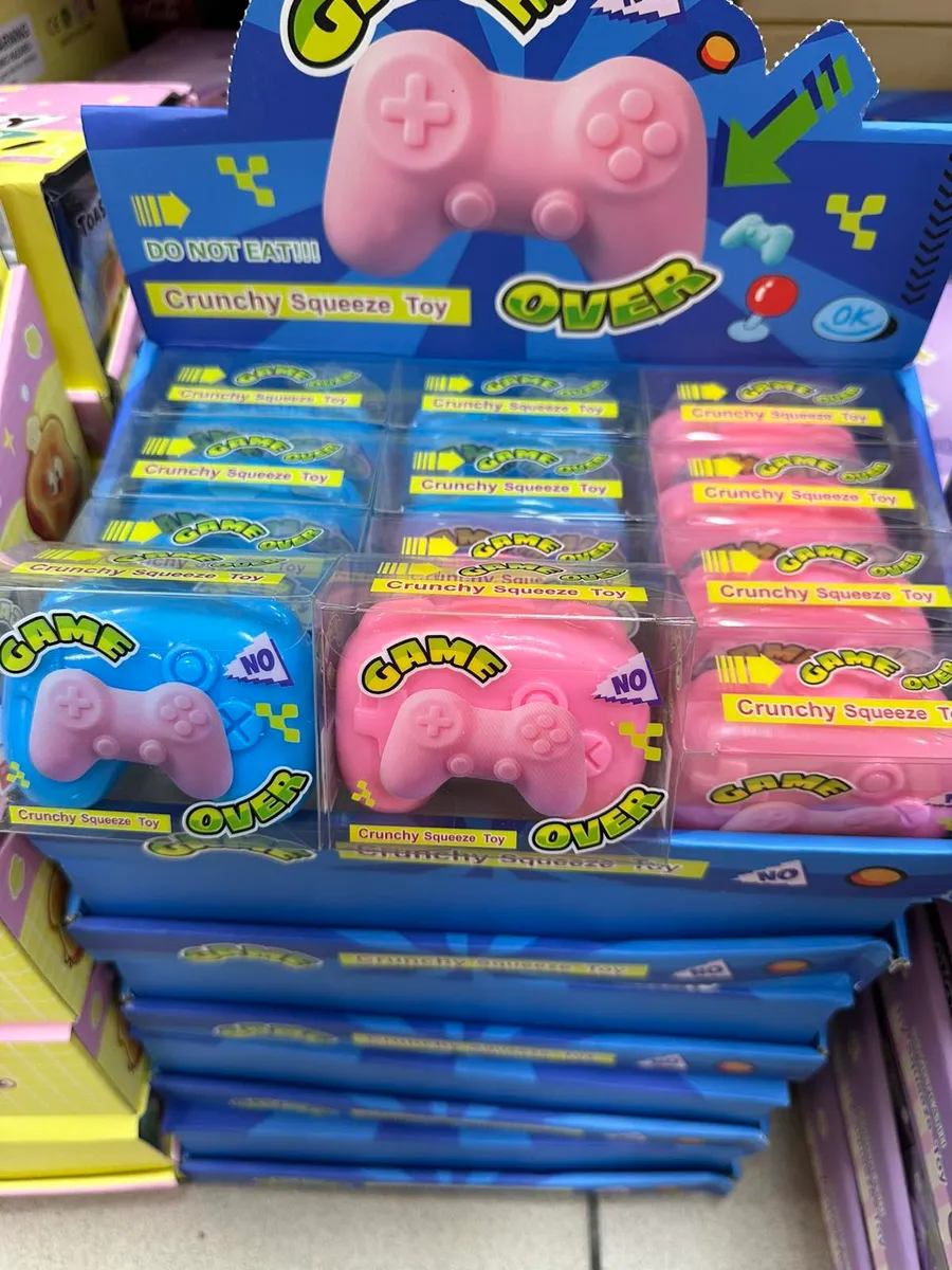 Zabawki Crunchy Squeeze w kształcie kontrolera do gier, różowe i niebieskie, w przezroczystych pudełkach na półce