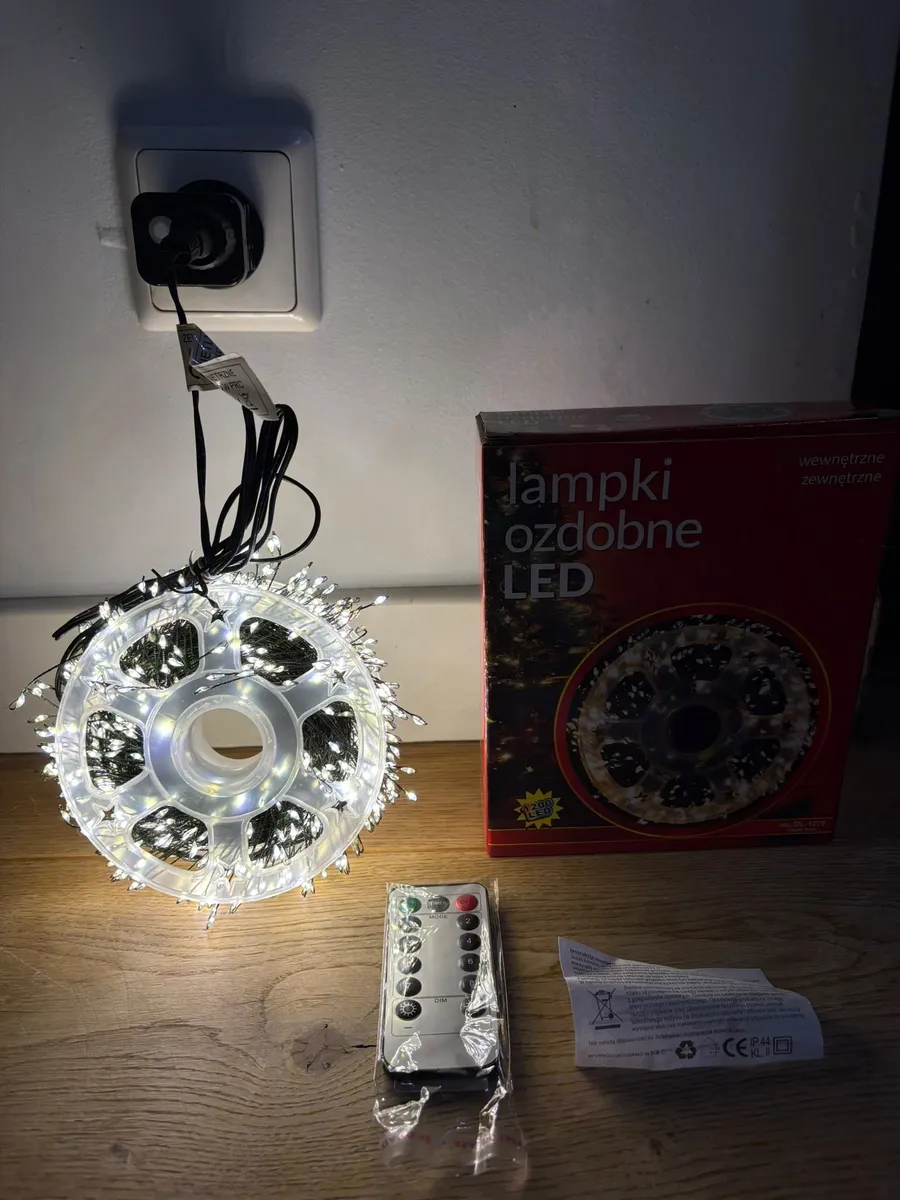 Lampki LED na zielonym druciku świecące ciepłym białym światłem, pilot i opakowanie na drewnianym stole