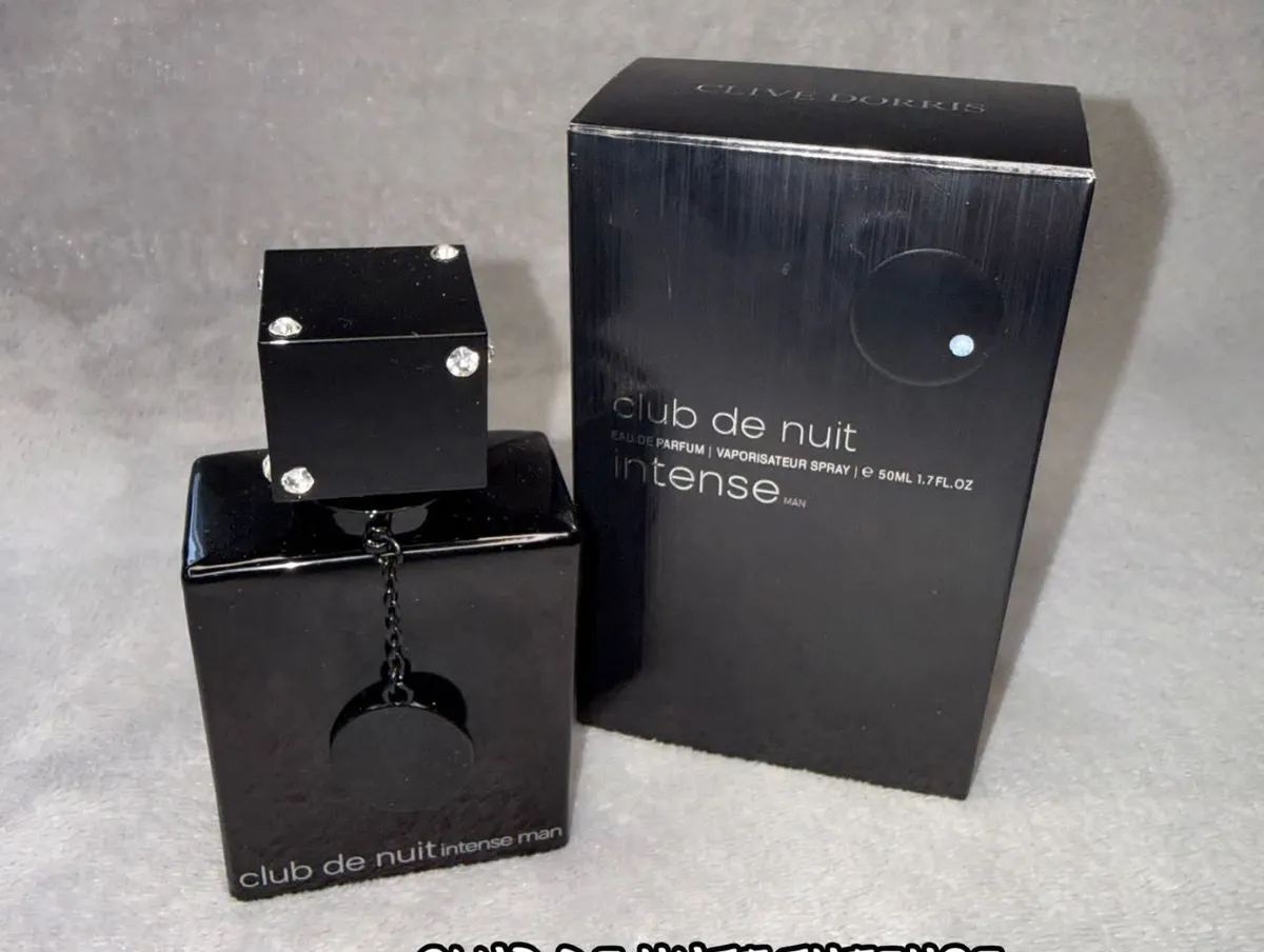 czarny flakon perfum Club de Nuit Intense Man 50ml z ozdobnym łańcuszkiem i kryształkami obok czarnego pudełka