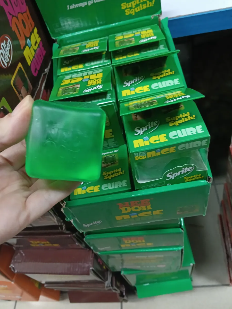 zielona przezroczysta kostka antystresowa z logo Sprite trzymana w dłoni na tle opakowań