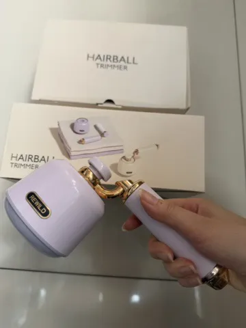 Golarka do ubrań Hairball Trimmer biała z złotymi elementami trzymana w dłoni, opakowanie w tle