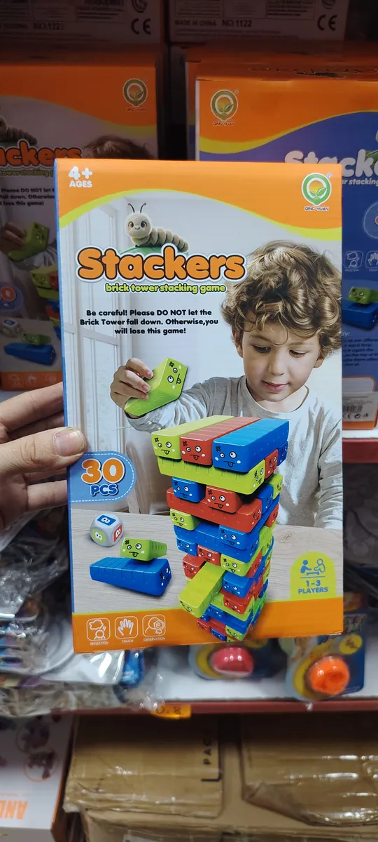 Opakowanie gry Stackers z kolorowymi drewnianymi klockami i dzieckiem układającym wieżę