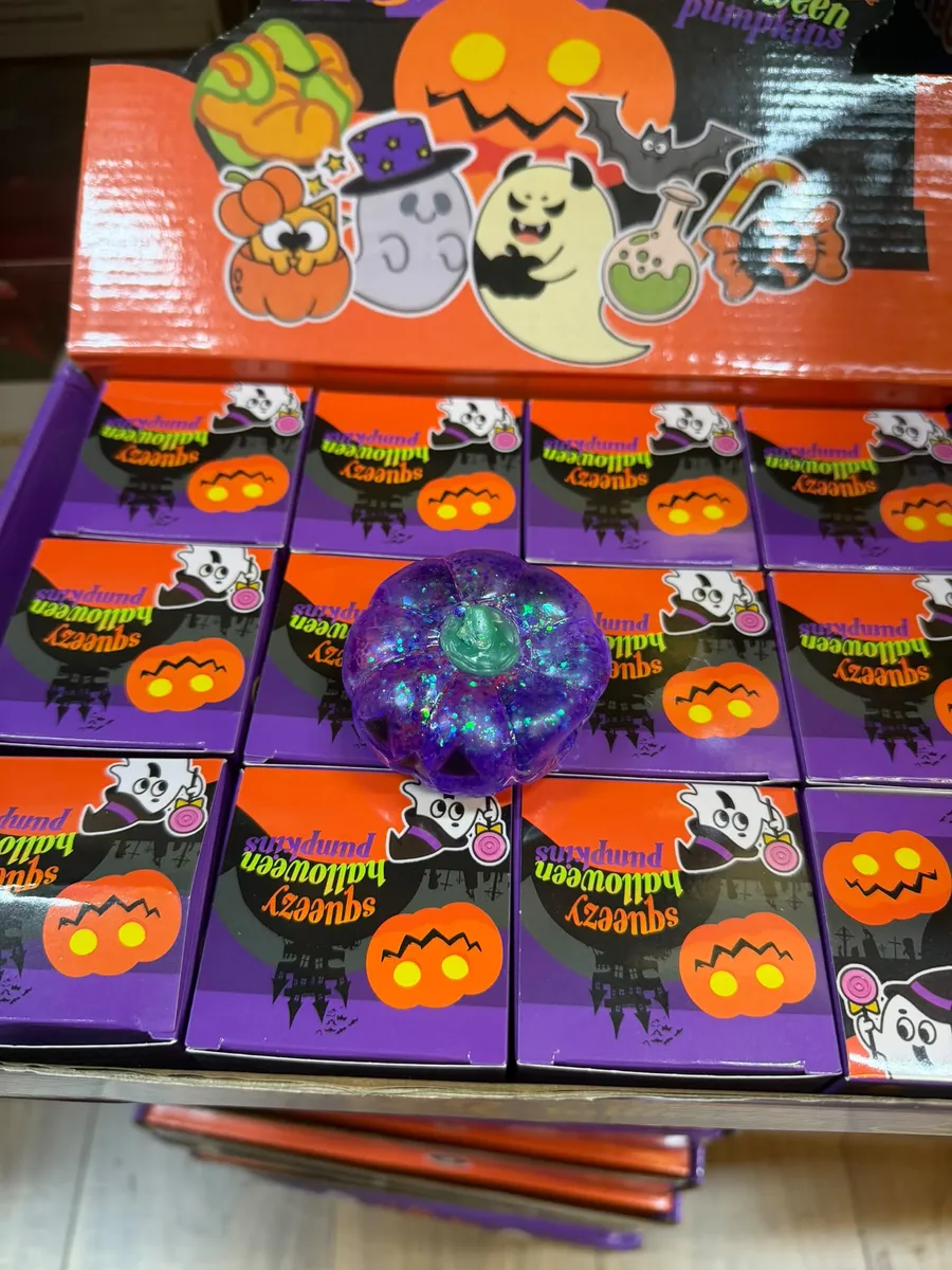 Fioletowa świeca w kształcie dyni z brokatem na tle opakowań z motywem Halloween
