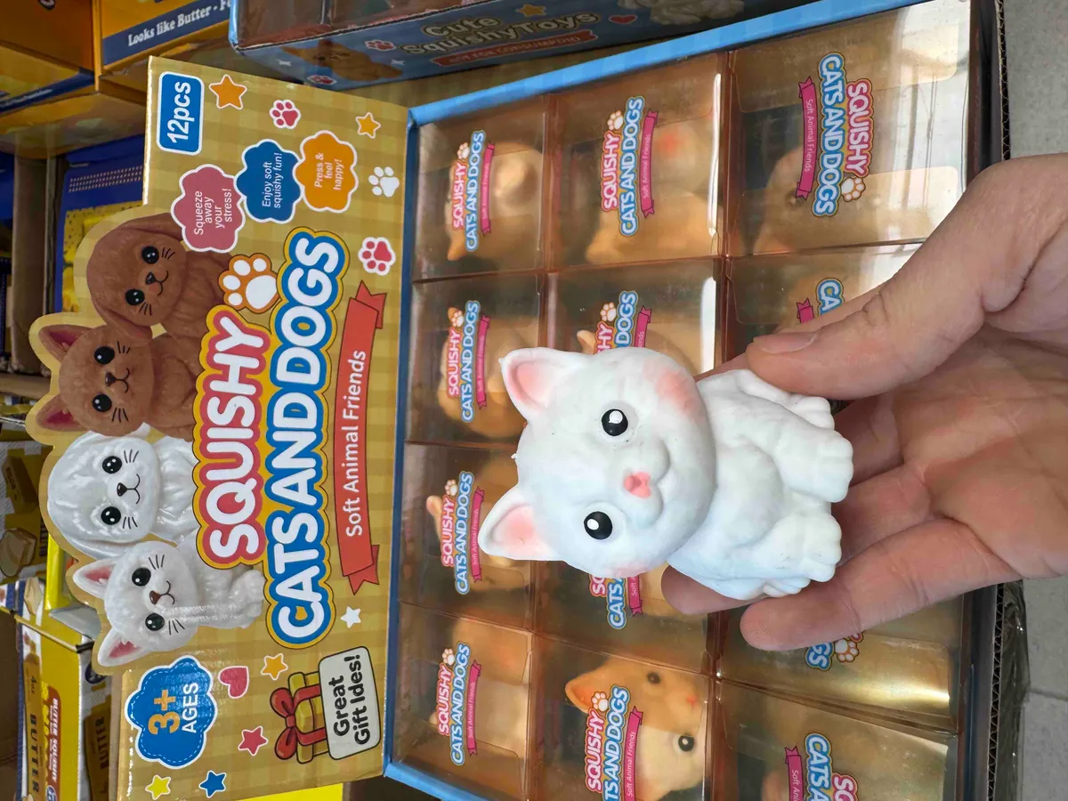 Miękka zabawka squishy w kształcie białego kota trzymana w dłoni na tle opakowania z 12 sztukami