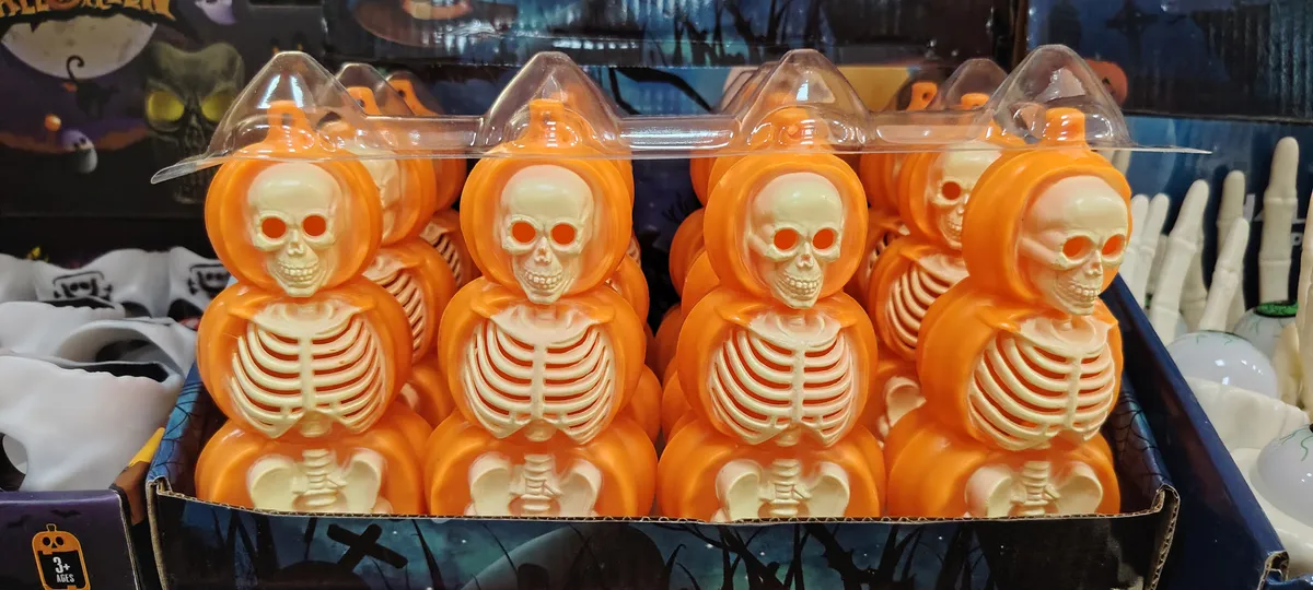 Figurki szkieletów w pomarańczowych dyniach ułożone w opakowaniu zbiorczym