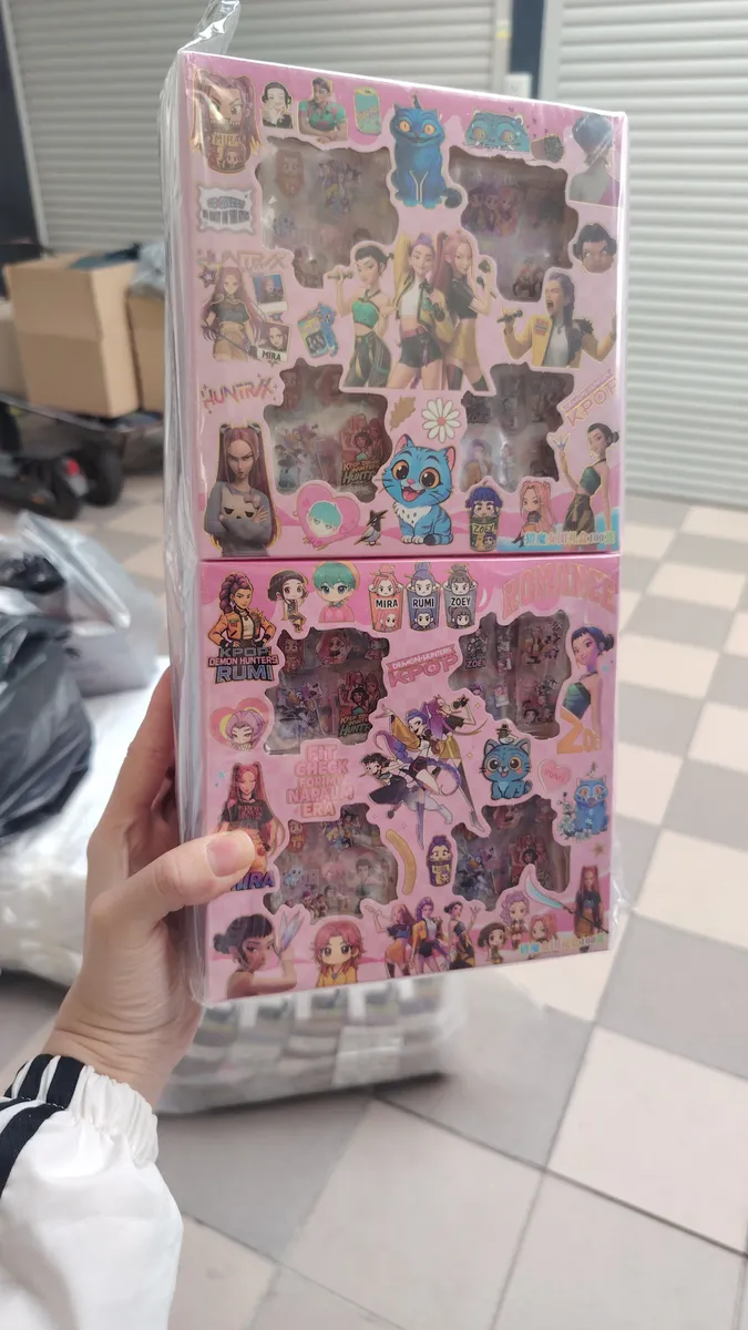 Ręka trzymająca różowy zestaw figurek K-POP Demon Hunters Rumi z kolorowymi grafikami