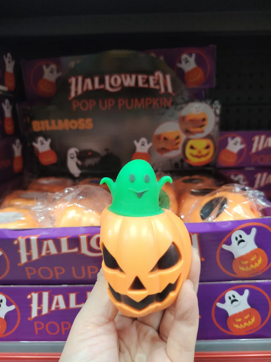 Pomarańczowa świecąca dynia z czarnymi oczami i zielonym duchem na szczycie, opakowanie fioletowe z napisem Halloween