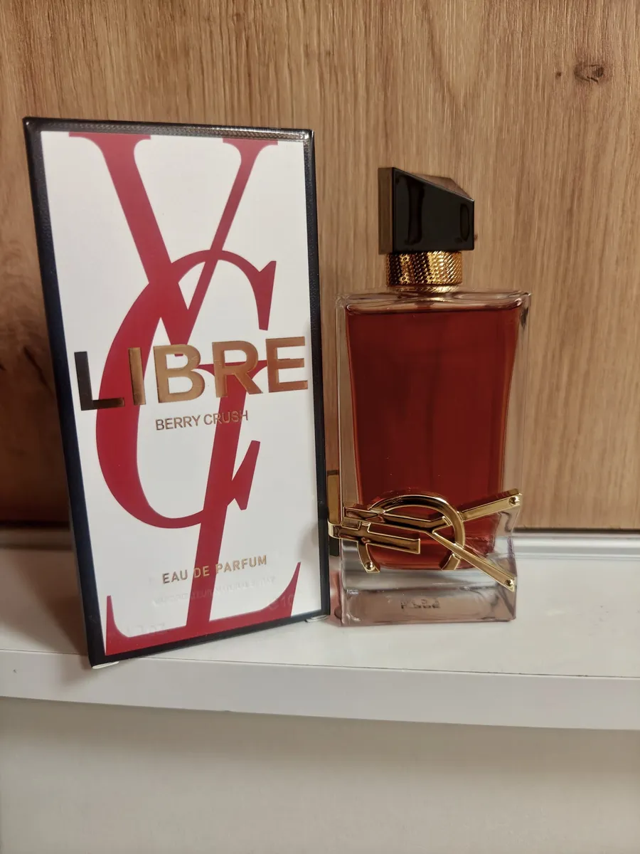 Flakon perfum Libre Berry Crush z bordowym płynem i złotym logo obok białego opakowania z czerwonymi literami