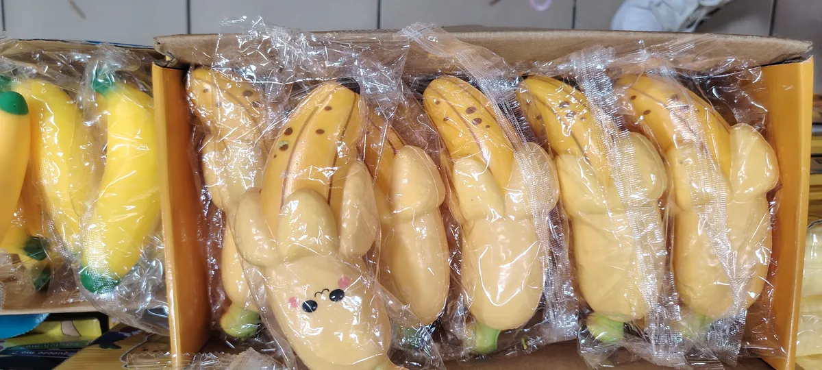 Miękka zabawka w kształcie żółtego banana z uśmiechem i zielonymi końcówkami, zapakowana w folię