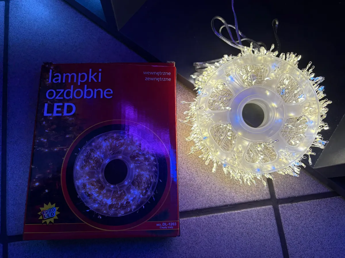 Lampki choinkowe LED na białym druciku zwinięte na plastikowej szpuli obok czerwonego opakowania