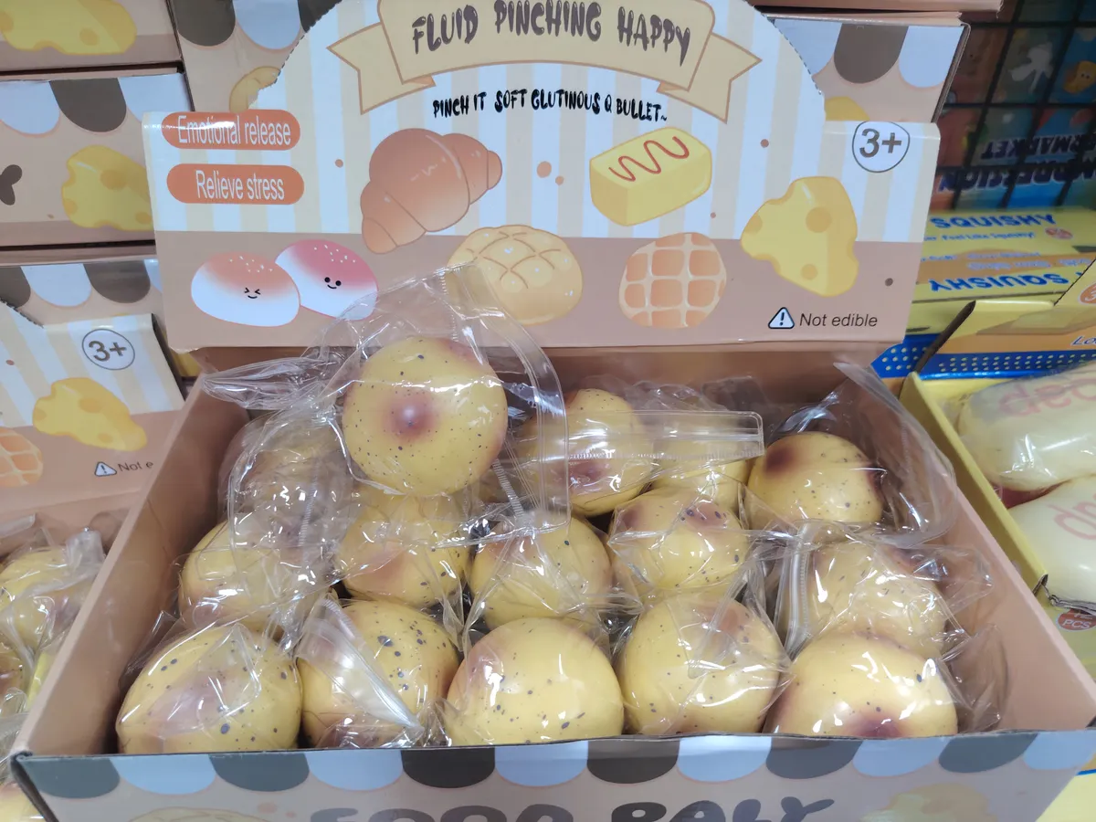 Miękka piłeczka squishy w kształcie bułki z brązowymi plamkami, zapakowana pojedynczo w folię