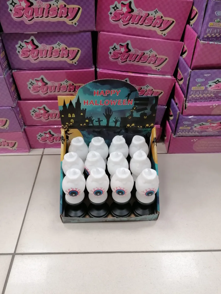 Białe figurki oka z niebieską tęczówką i czerwonymi żyłkami na czarnej podstawie w kartonie z napisem Happy Halloween
