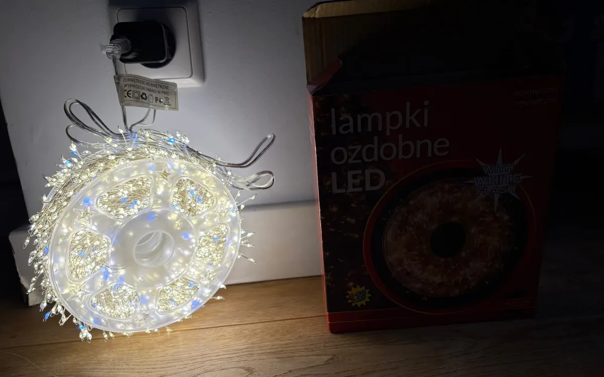 Lampki choinkowe LED na białym druciku z diodami świecącymi ciepłym białym i białym flash, nawinięte na bębenek obok opakowan