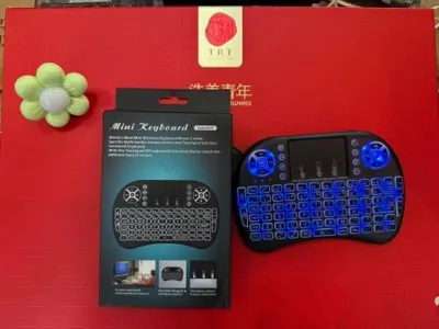 Mini czarna klawiatura bezprzewodowa z niebieskim podświetleniem LED i touchpadem obok pudełka produktu