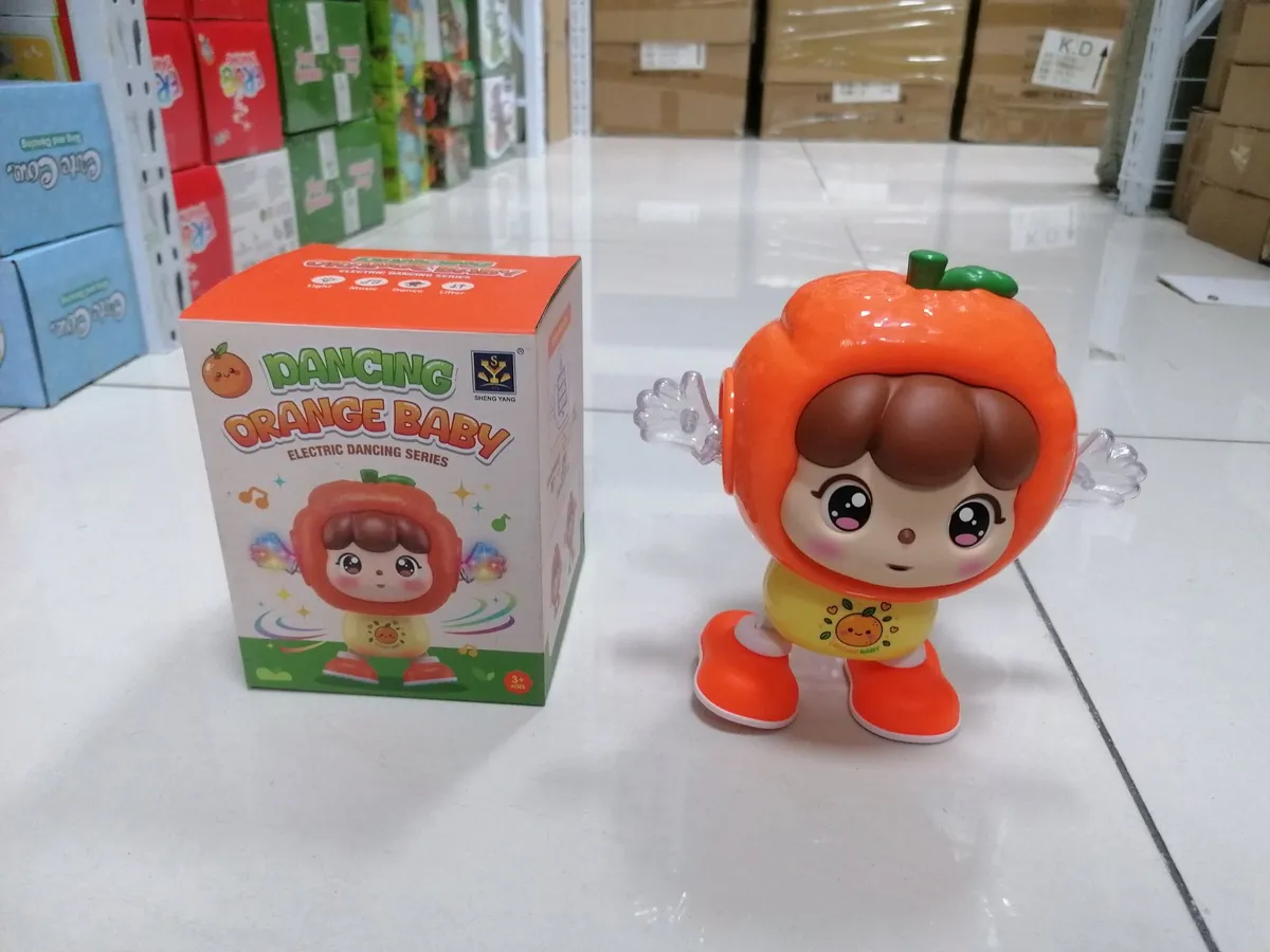pomarańczowa zabawka Dancing Orange Baby z ruchomymi rękami i opakowaniem na białej podłodze