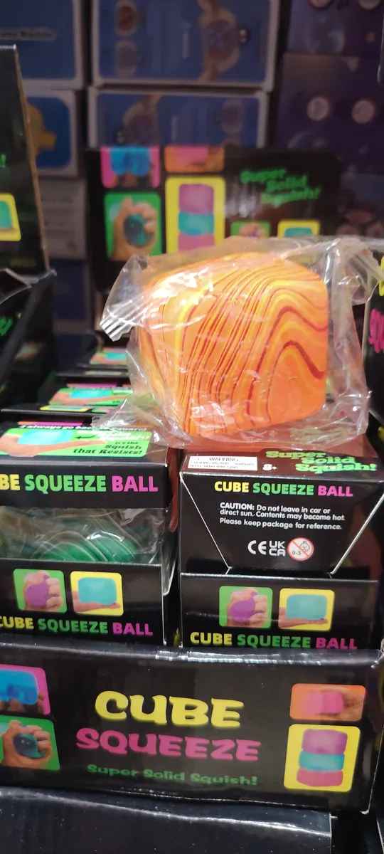 Pomarańczowa kostka antystresowa Cube Squeeze Ball z wzorem w folii na tle opakowań